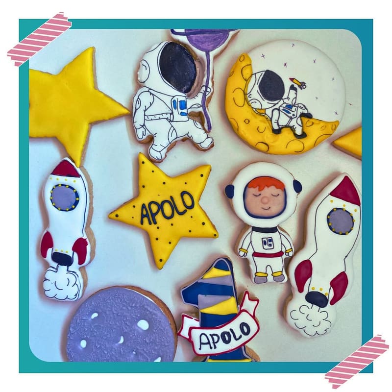 Biscoitos decorados com tema espacial: astronauta, foguete, lua, planeta e estrela amarela com a palavra Apolo