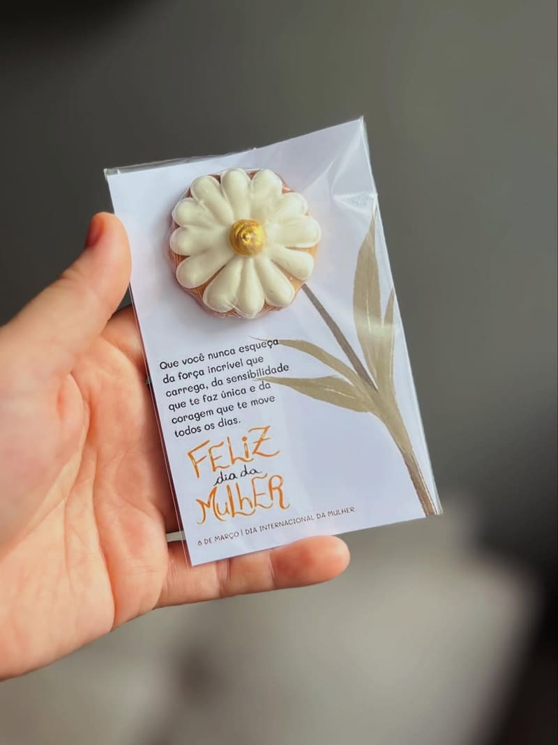 Biscoito em formato de margarida ao lado de um cartão impresso, segurado na mão