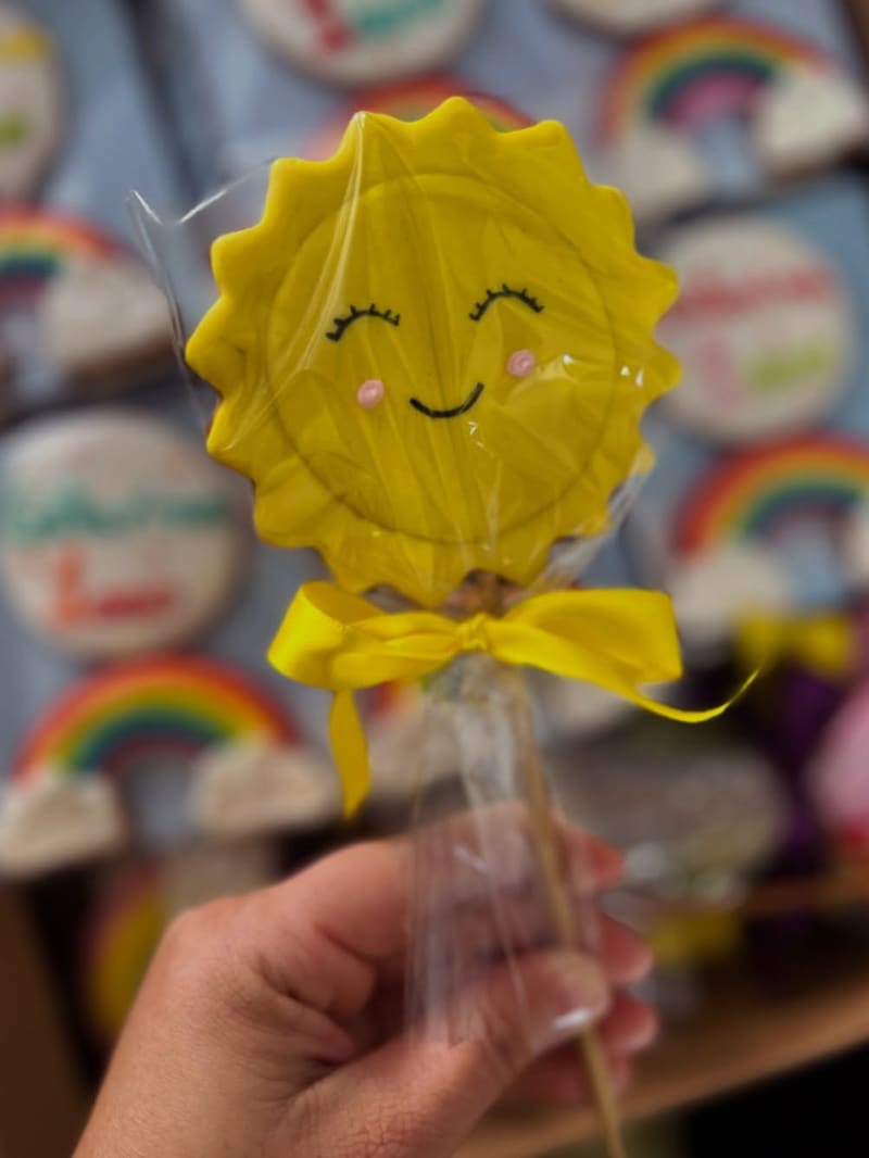 Detalhe de um biscoito decorado em formato de sol, segurado na mão, mostrando o relevo do glacê