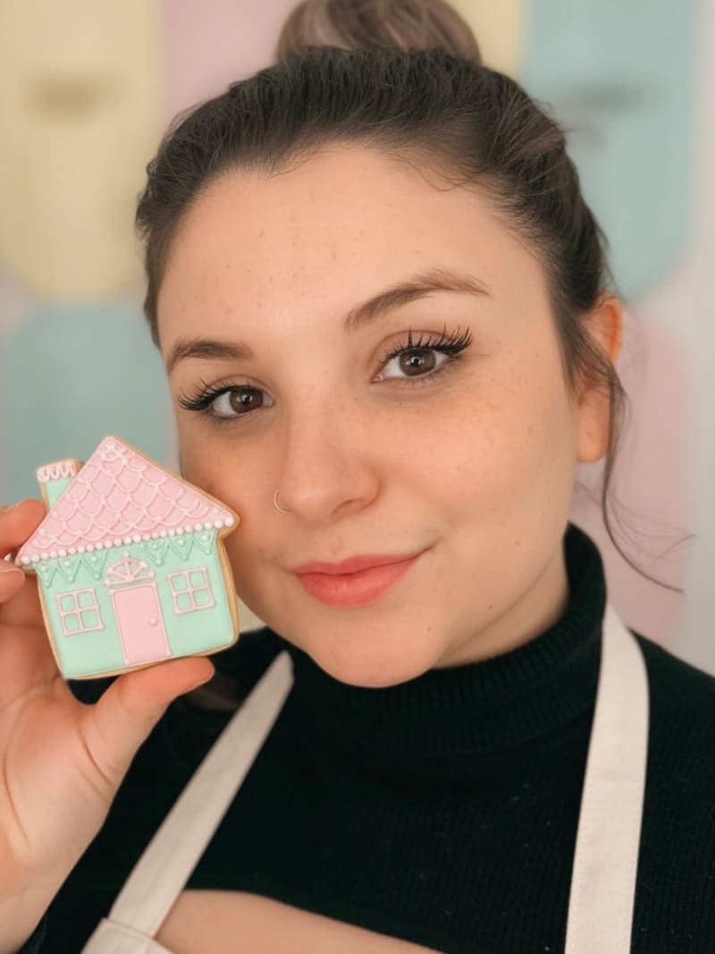 Juliana Vieira sorrindo enquanto segura um biscoito decorado em formato de casinha